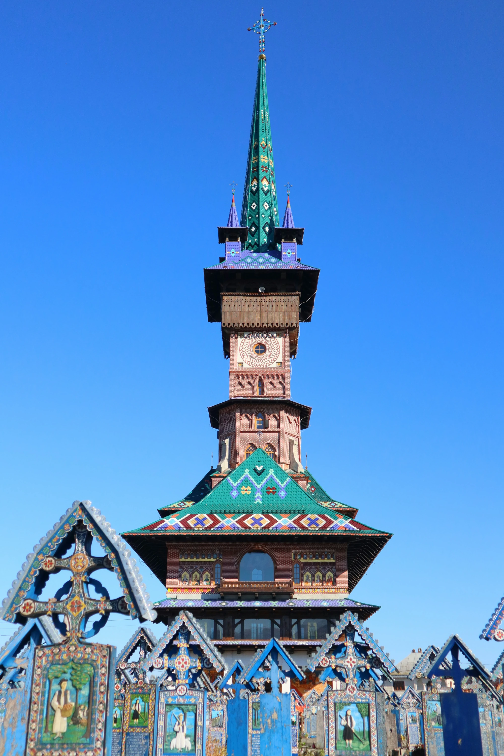 Colorful wooden crosses at the Merry Cemetery of Săpânța and the tall wooden church tower